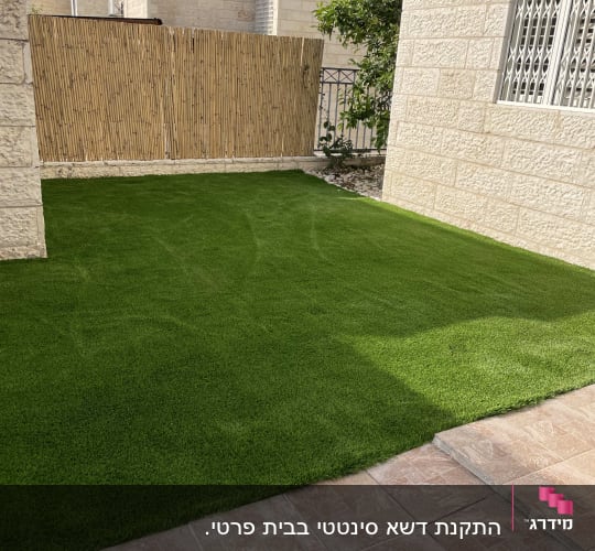 דשא ירוק עם גדר במבוק ועץ קטן